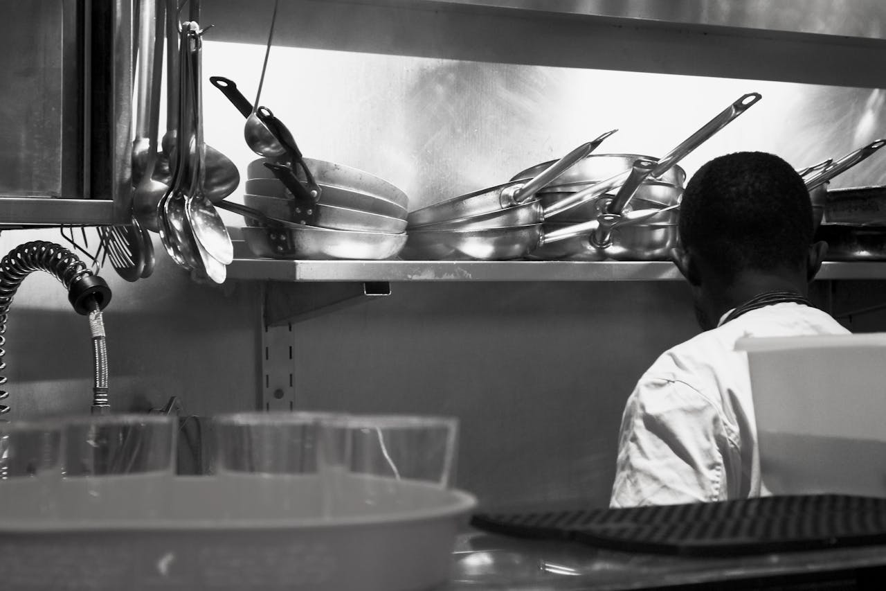 Black and white photo of a chef in a kitchen with metal pans and utensils.